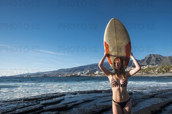 Caucasian woman standing on beach holding surfboard