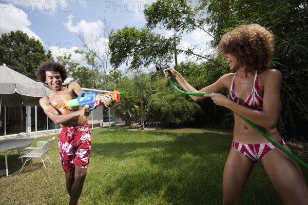 Couple squirting each other with water in backyard