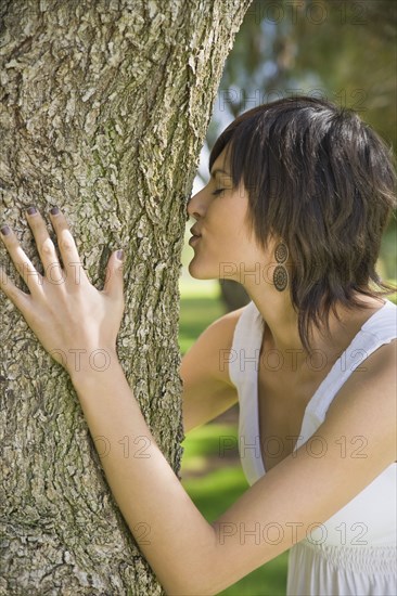 Hispanic woman hugging tree trunk