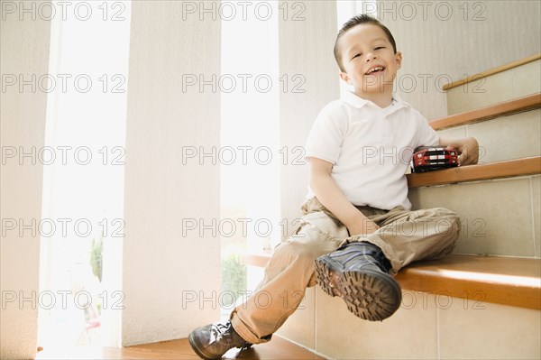 Hispanic boy sitting on staircase with toy car