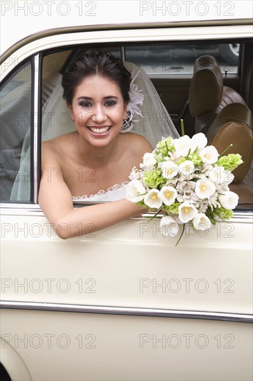 Hispanic bride sitting with bouquet in back of car