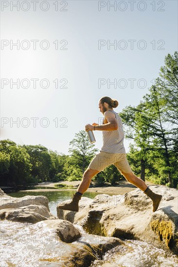 Caucasian man jumping on rocks near river