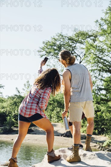 Friends posing for cell phone selfie on rocks near river