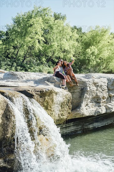 Friends posing for cell phone selfie on rocks near waterfall