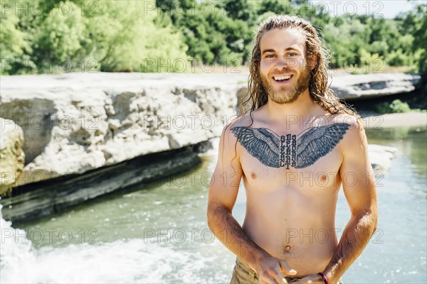Smiling Caucasian man with chest tattoo standing near river