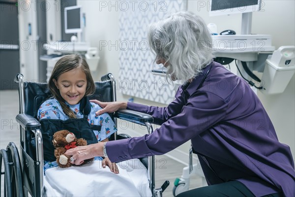 Doctor giving teddy bear to girl in wheelchair