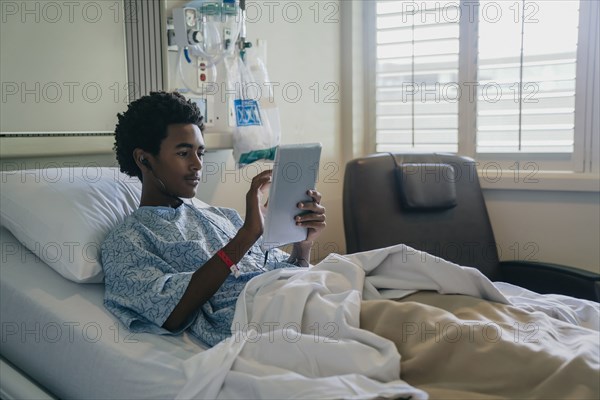 Black boy in hospital bed listening to digital tablet