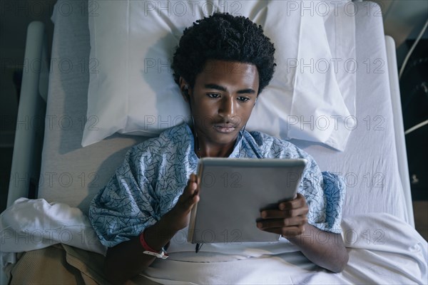 Black boy in hospital bed listening to digital tablet