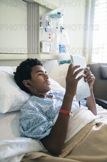 Black boy in hospital bed listening to digital tablet