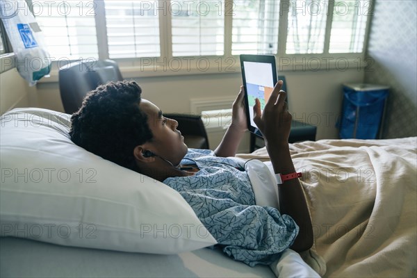 Black boy in hospital bed listening to digital tablet