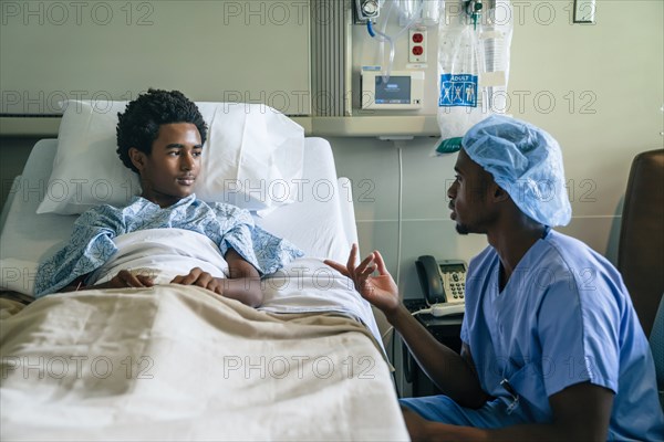 Black nurse talking to boy in hospital bed