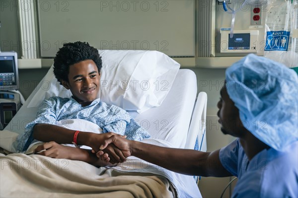 Black nurse shaking hands with boy in hospital bed