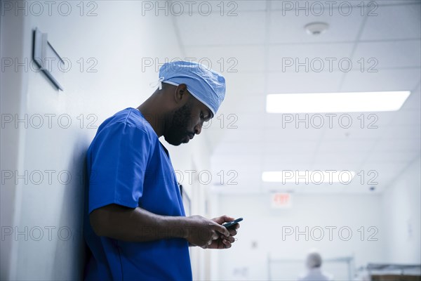 Black nurse leaning on wall texting on cell phone