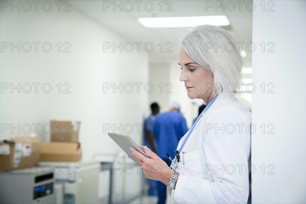 Caucasian doctor leaning on wall using digital tablet