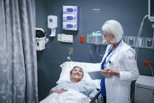 Doctor with digital tablet talking to smiling patient in hospital