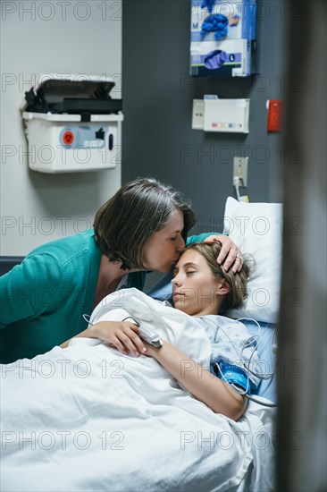 Mother kissing forehead of daughter in hospital bed