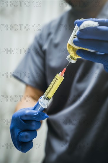 Mixed race nurse wearing rubber-gloves holding medicine and needle