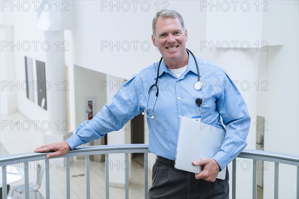 Portrait of smiling Caucasian doctor leaning on railing holding laptop