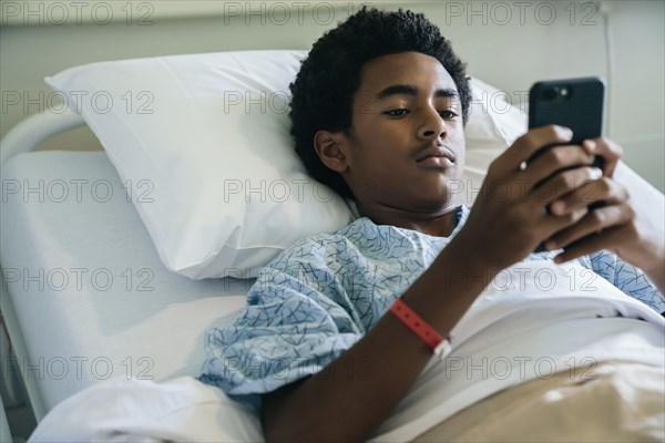 Black boy laying in hospital bed texting on cell phone