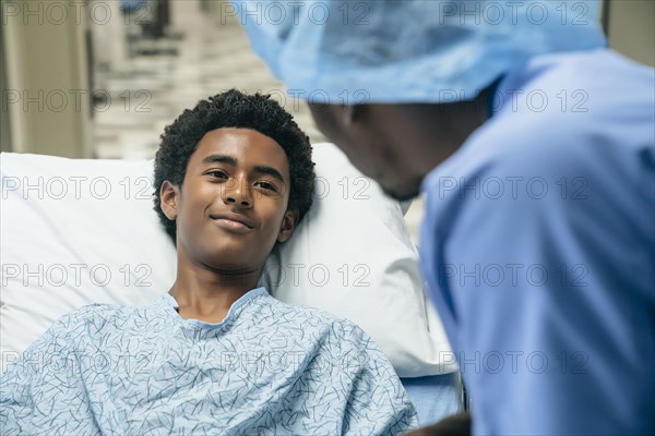 Black doctor talking to boy in hospital bed