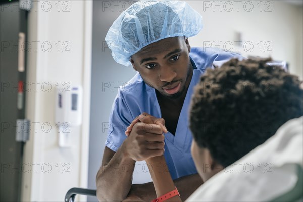 Black doctor holding hand of boy in hospital bed