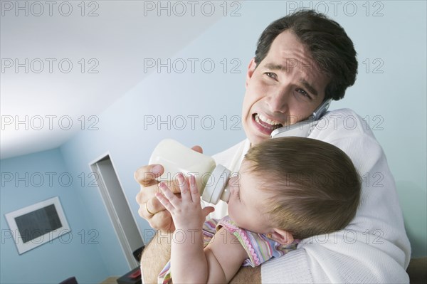 Stressed Hispanic father feeding baby