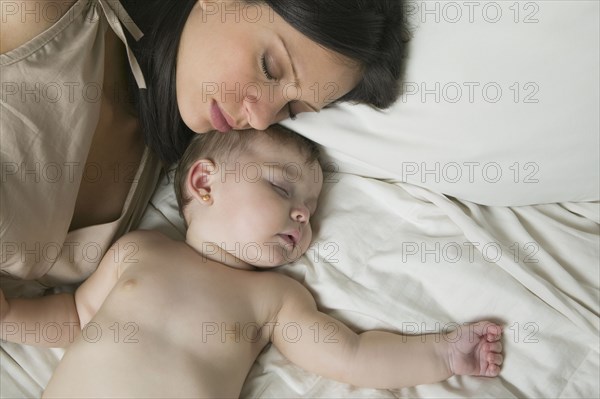 Hispanic mother and baby sleeping on bed