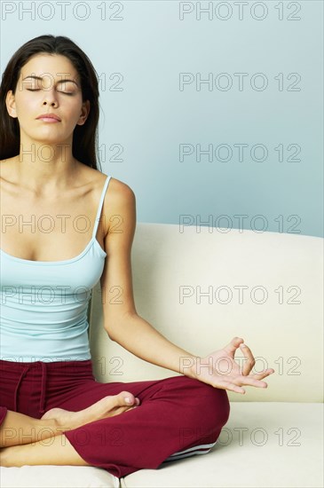 Hispanic woman meditating on sofa