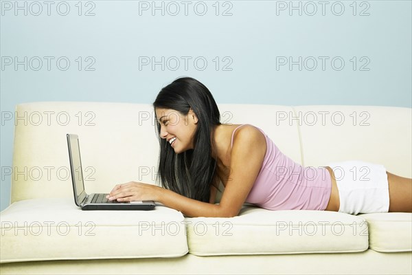 Young Hispanic woman using laptop on sofa