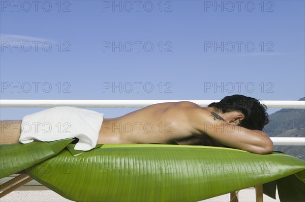 Asian man laying on spa table with banana leaves outdoors