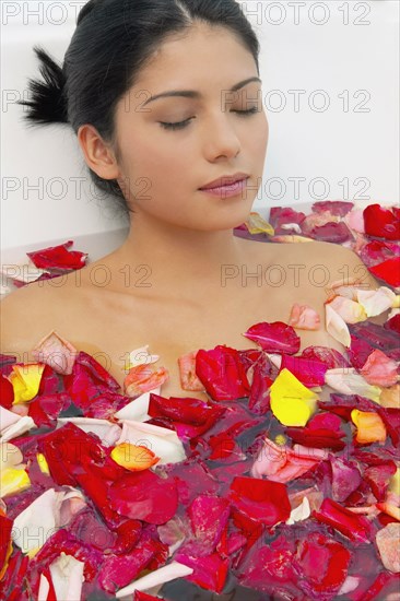 Hispanic woman with eyes closed in bath of flower petals