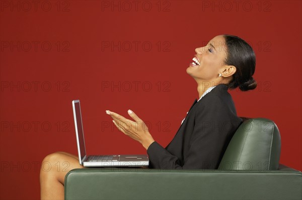 Profile of African businesswoman laughing with laptop in armchair