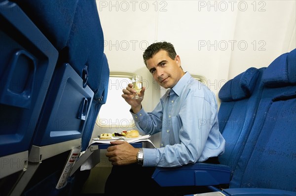 Man eating and toasting with wine on airplane