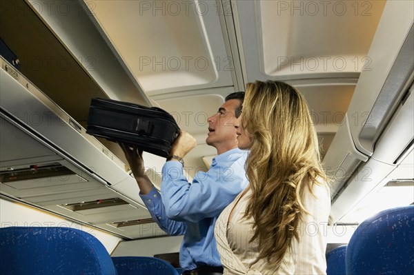 Couple stowing luggage in overhead compartment on airplane