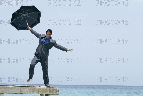 Hispanic businessman holding umbrella on dock