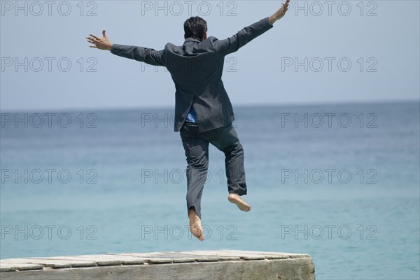 Hispanic businessman jumping off dock