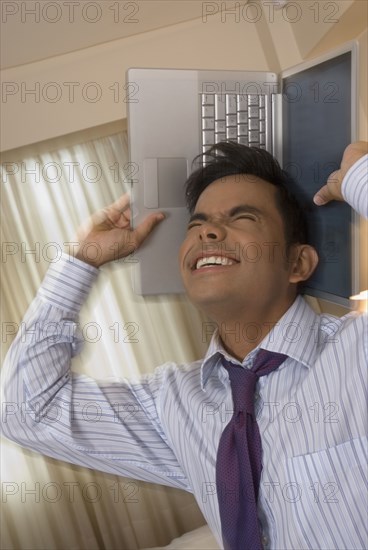 Hispanic businessman holding laptop around head