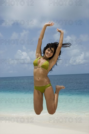 Hispanic woman jumping at beach