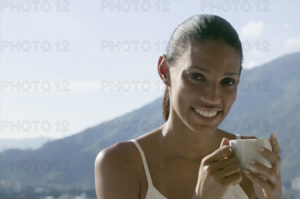 African woman drinking coffee with mountains in background