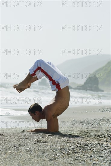 Hispanic man doing yoga at beach