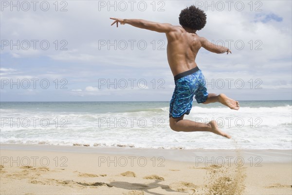 African man at beach jumping in mid-air