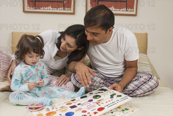 Hispanic parents reading book to daughter in bed