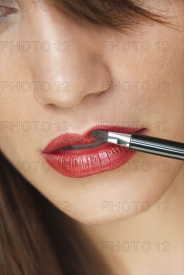 Caucasian woman putting on lipstick with brush
