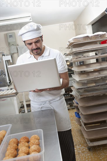 Hispanic baker working on laptop in commercial kitchen