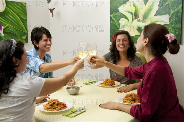 Hispanic friends toasting at dinner with white wine