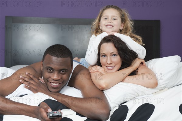 Family laying in bed together watching television