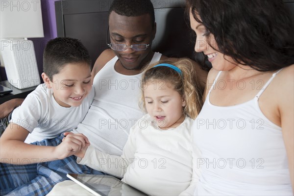 Family using digital tablet together in bed