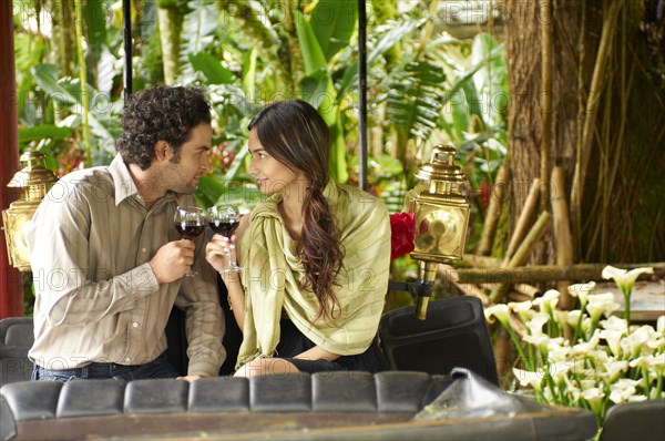 Hispanic couple sitting in carriage drinking red wine