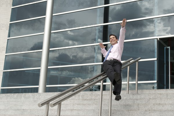 Hispanic businessman sliding down railing