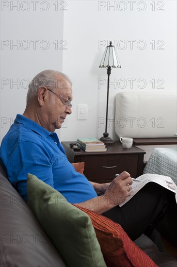 Senior Hispanic man sitting on sofa looking at newspaper